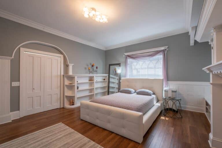Master bedroom suite with a bed, gray and white walls, nightstand, and mirror