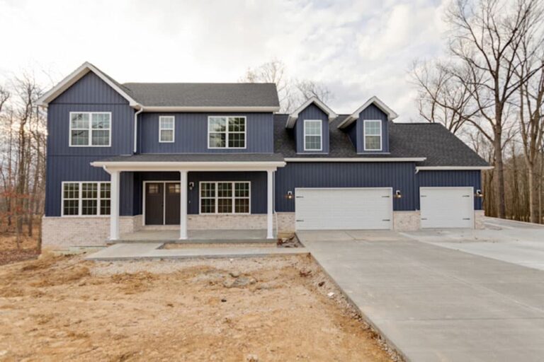 Modern blue home with spacious driveway, garage, and scenic natural surroundings.