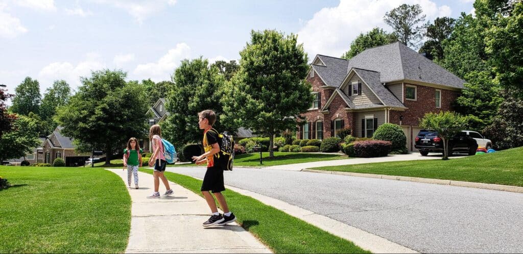 Children playing and walking in a suburban neighborhood on a sunny day.