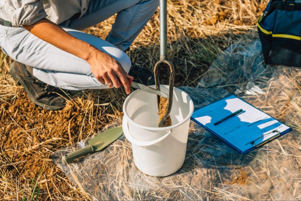 Scientist collecting soil samples for field research and analysis in a rural area.