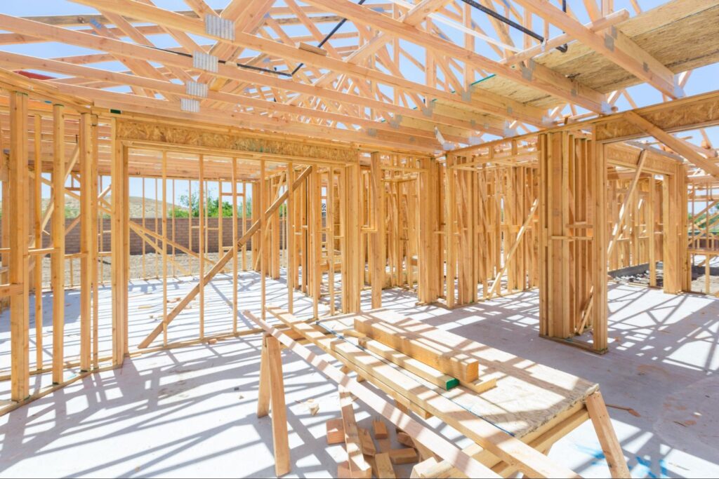 Framing structure of a new home under construction with wooden beams and bright sunlight.