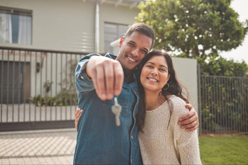 Happy couple holding house keys in front of their new home.