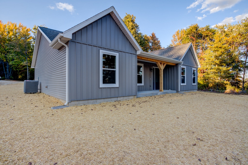 Modern gray house with a spacious yard surrounded by trees and blue sky.