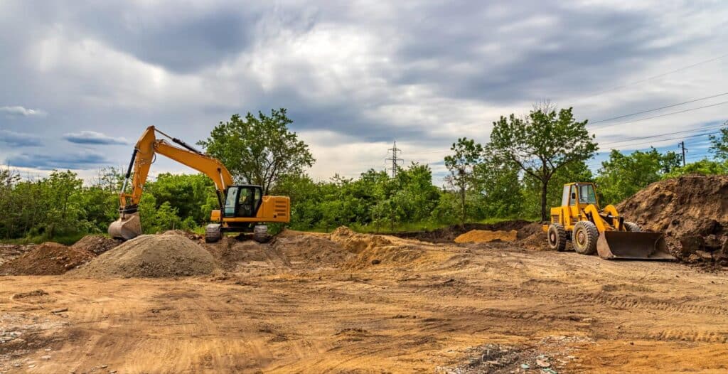 Excavators and loaders actively working at a construction site with cloudy skies.