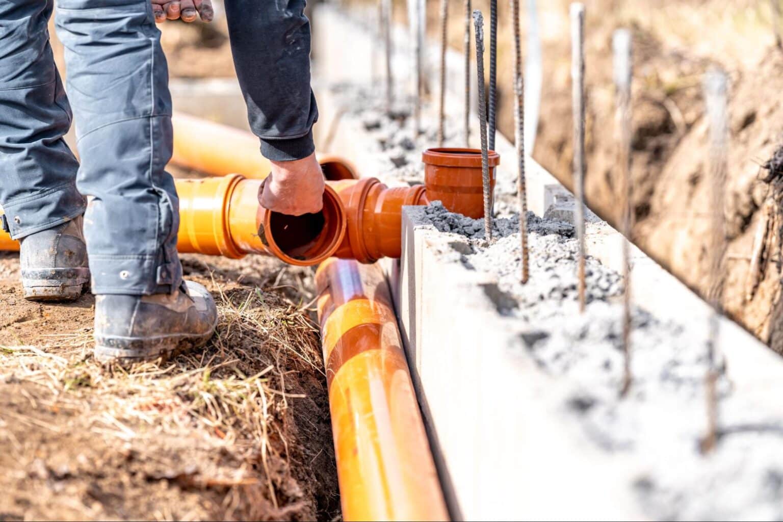 Worker installing orange drainage pipes at a construction site.