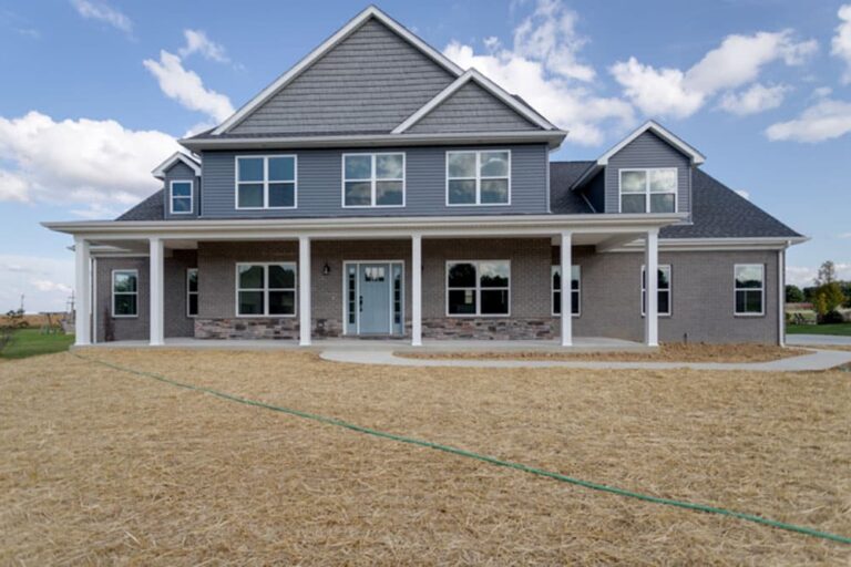 Modern two-story home with a stylish exterior, expansive porch, and landscaping ready for finishing.