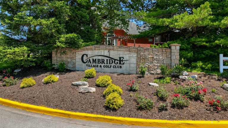 Cambridge Village Golf Club entrance surrounded by vibrant landscaping and trees.