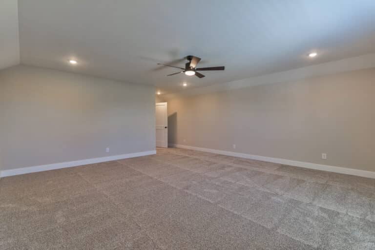 Spacious empty room with a ceiling fan and soft carpeted flooring.
