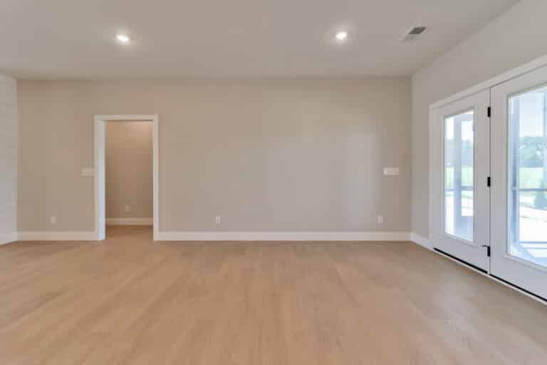 Spacious empty room with wooden flooring and bright natural light through large windows.
