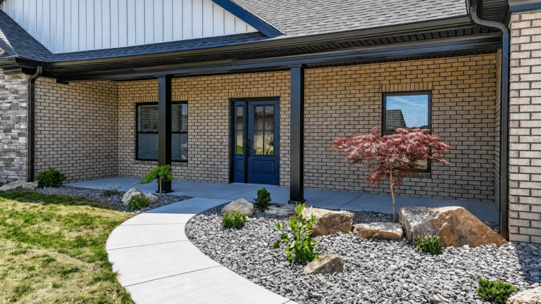 Charming front entrance with beautiful flowers and landscaped rocks surrounds a welcoming blue door.