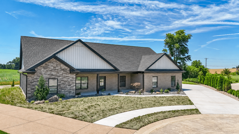Modern house exterior with landscaped yard and driveway under a clear blue sky.