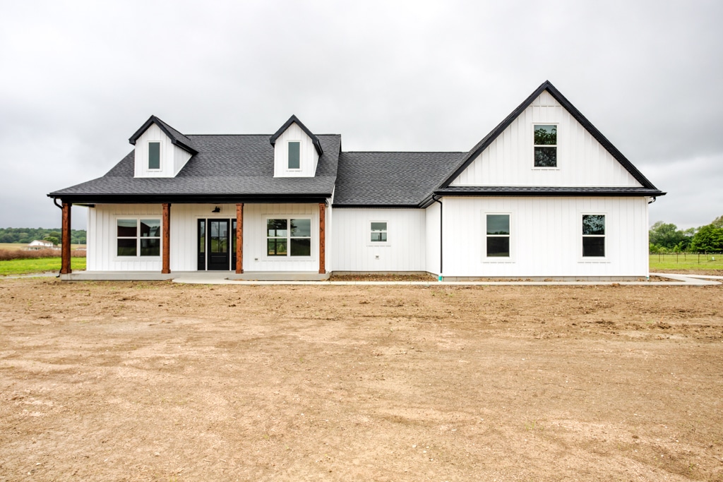 Modern farmhouse exterior featuring large windows and a spacious landscape.