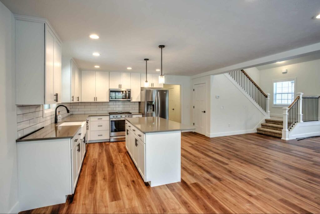 Stylish open concept kitchen with white cabinets and hardwood floors, perfect for gatherings.
