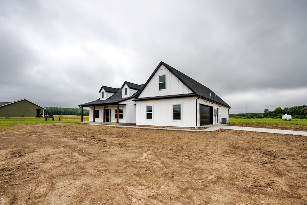 Modern farmhouse with black roof and expansive land, featuring a stylish design.