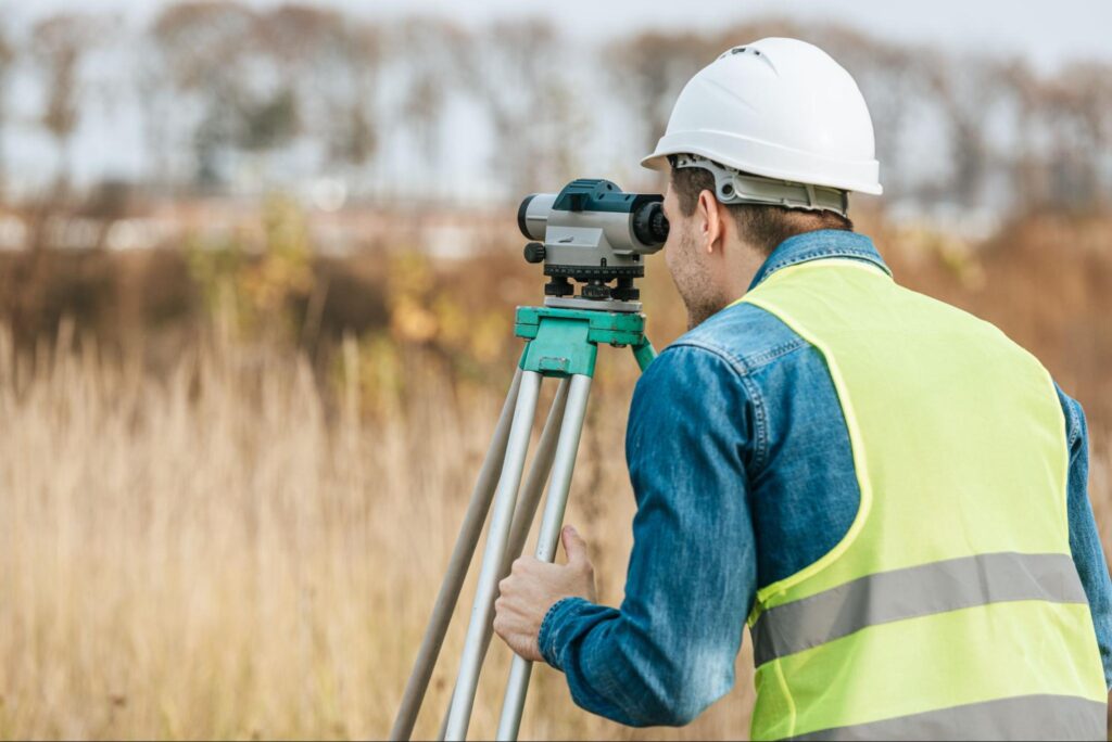 Surveyor using a theodolite for precise land measurements in a construction area.