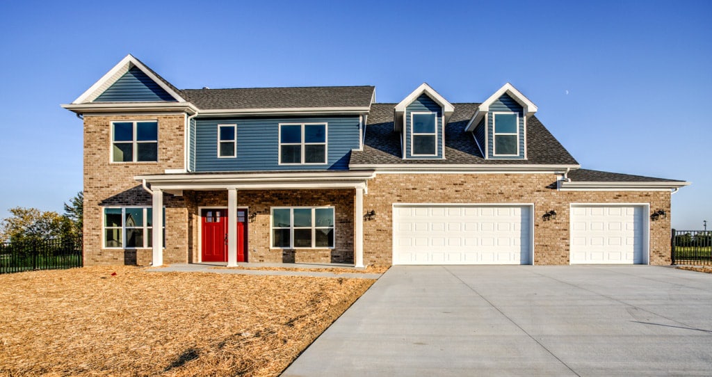 Stunning brick home featuring a red door and spacious driveway on a bright day.