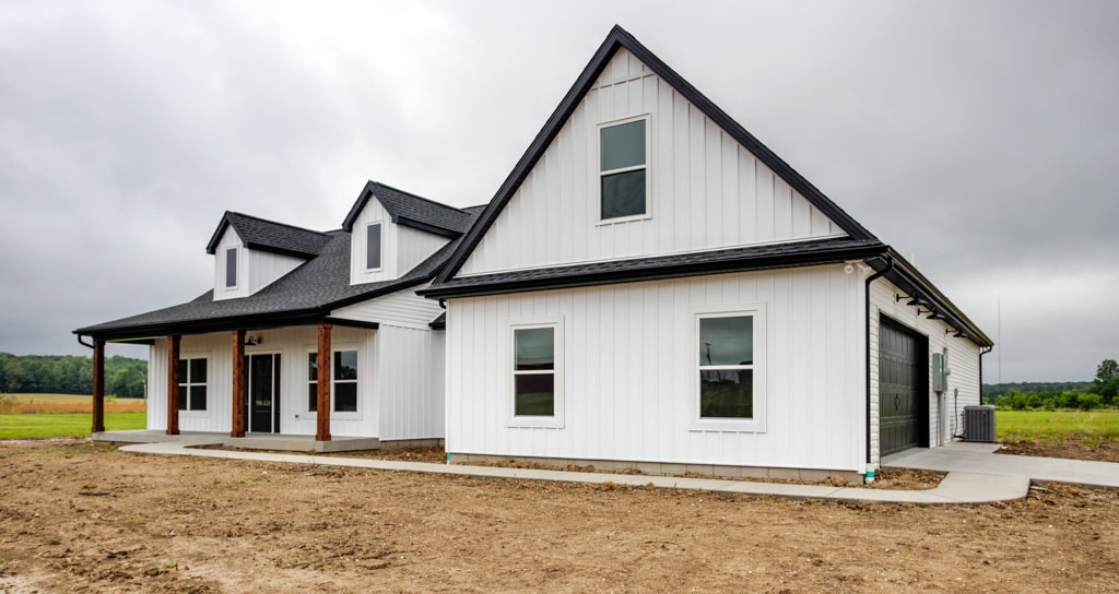 Stylish modern farmhouse with white siding and gray roof amid scenic fields.
