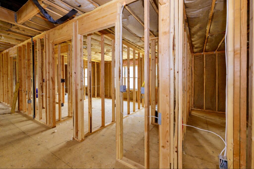 Progress of house framing with wooden studs and exposed electrical wiring.