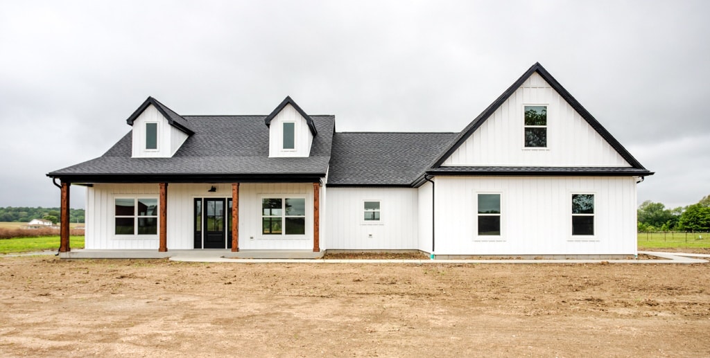 Modern farmhouse exterior featuring white siding and a black roof in a rural setting.